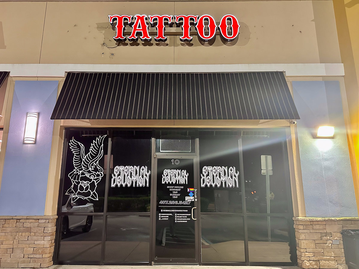 outside of tattoo shop with red sign and black glass windows